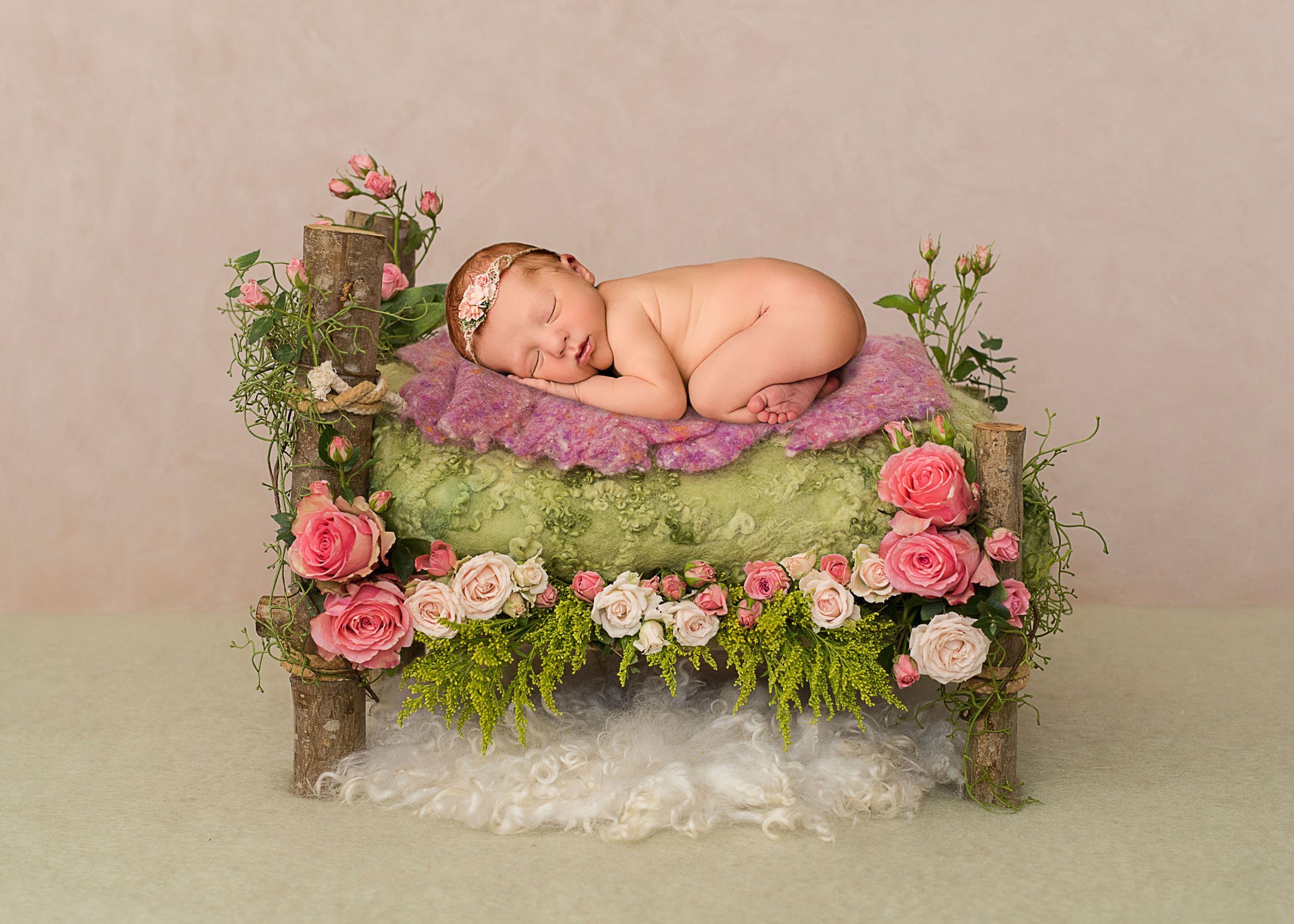 newborn baby girl sleeping on timber bed decorated with pink roses
